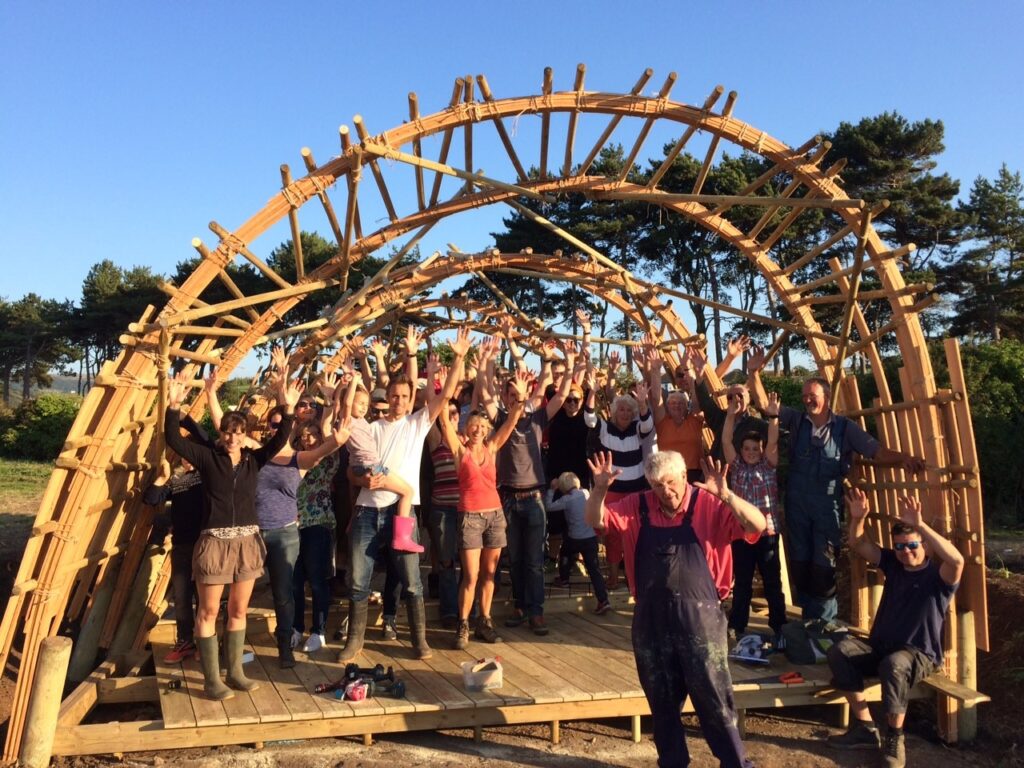 Onion Collective community building project. Lots of people waving under a wooden arch.