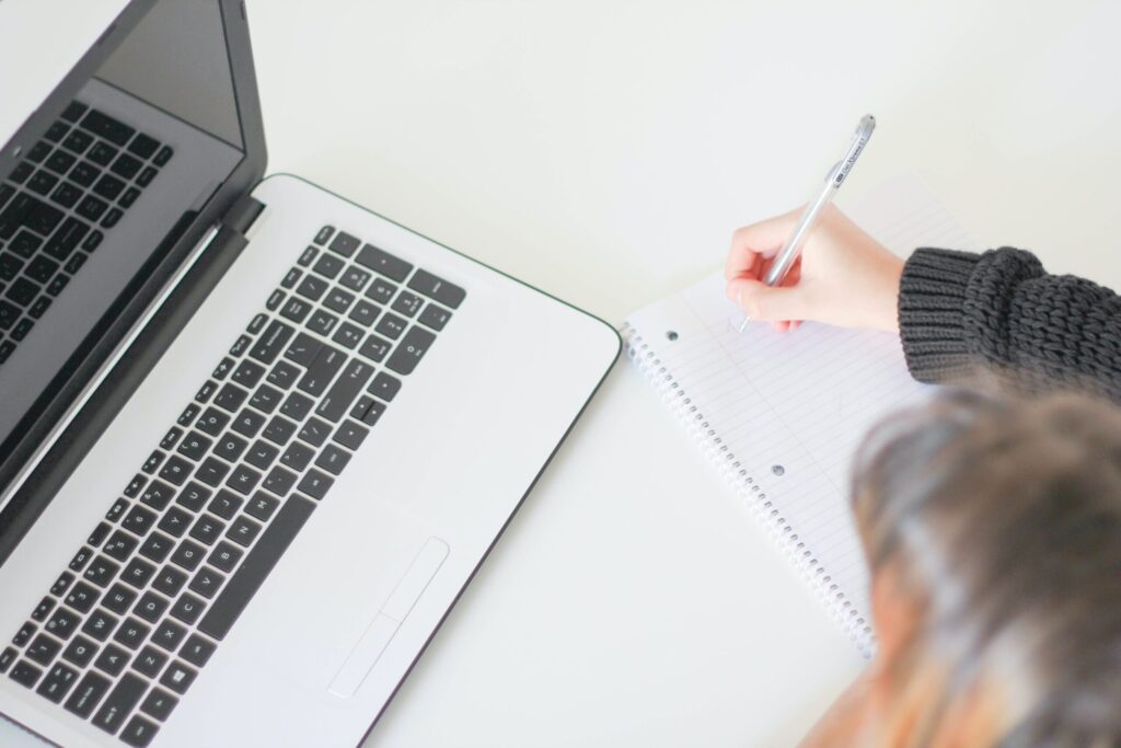 laptop and woman making notes beside it
