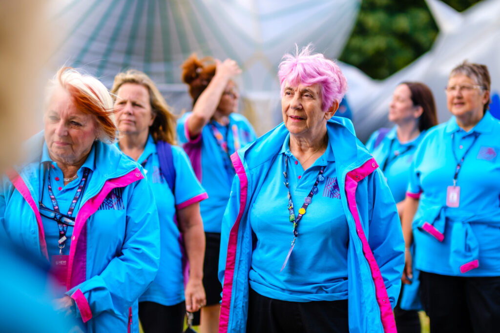A group of Olympics volunteers wearing their blue jackets and lanyards. The woman at the front has pink hair.